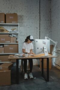 Woman in a warehouse setting organizing packages on a desk, showcasing logistics and office work.