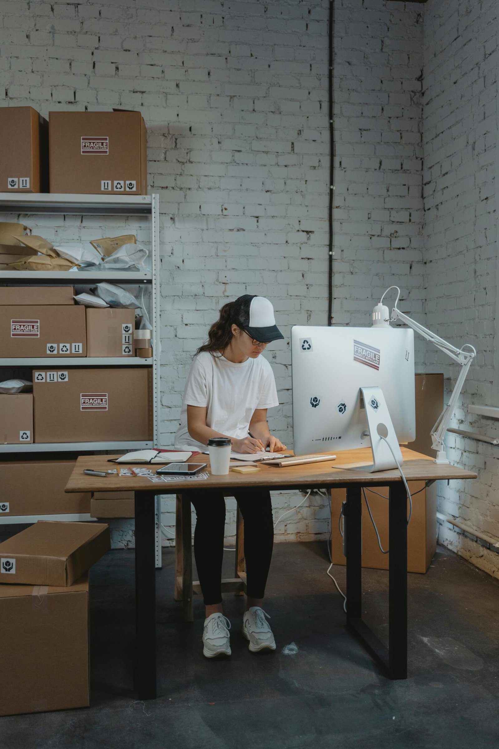Woman in a warehouse setting organizing packages on a desk, showcasing logistics and office work.